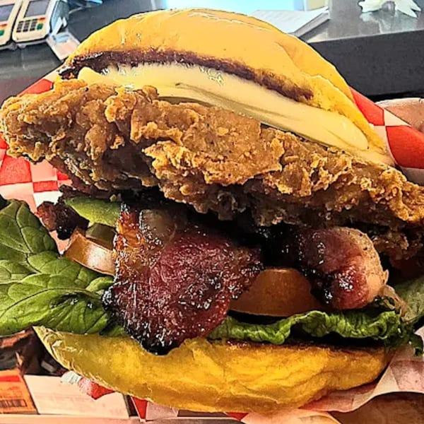 A close-up of a Sno-White Drive In fried chicken sandwich with bacon, lettuce, and tomato.